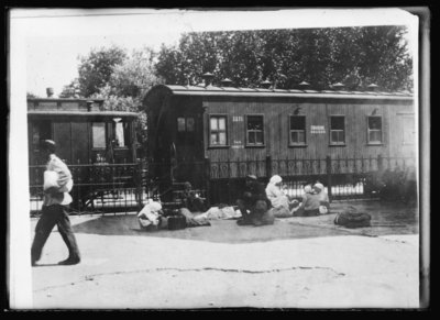 A family group in a railroad station waiting for a train. Although there is a nominal schedule for the departure of trains, in reality they leave only as the traffic warrants. The philisophical Russian peasant brings his wife and children and bundles to the Depot Compound and there they sit, eat and sleep often for two days and sometimes a week until they find a train and, what is more important, a place upon that train to reach their destination